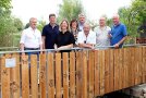 Acht Männer und Frauen stehen auf einer Holzbrücke im Schau- und Lehrgarten in Petersaurach. Sie sind gekommen, um bei einem Fest für die neue Brücke mitzufeiern und das Bauwerk einzuweihen.