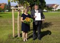 Hans Popp hält die Staatsmedaille und die Urkunde. Neben ihm steht seine Frau mit Blumen.