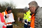 Vier Männer stehen an einem Bach in der Nähe von Oberndorf und schauen sich die Flächen darum herum an, ob an der Stelle Maßnahmen zum Schutz nach Unwettern Sinn machen. Sie haben auch eine Karte vom Gebiet dabei.