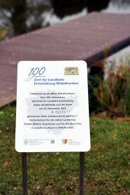 Eine Tafel am Klosterweiher in Heilsbronn erinnert an den 100. Geburtstag des Amts für Ländliche Entwicklung Mittelfranken. Der Baum steht für alle Menschen im ländlichen Raum Mittelfrankens.