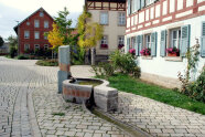 Der Dorfplatz in Auernhofen ist mit Sitzmöglichkeiten und Brunnen der Mittelpunkt der kleinen Ortschaft. Darum herum stehen viele Gebäude mit schmuck sanierten Fassaden.