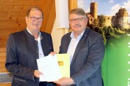 Zwei Männer stehen in Burgthann im Sitzungszimmer des Rathauses und freuen sich mit einem Zuwendungsbescheid für ein Pressefoto über EU-Fördermittel.