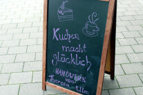 Eine Tafel steht vor einem Discounter in Leutershausen. Darauf steht „Kuchen macht glücklich“ mit lila Kreide geschrieben. Es wirbt für Theresa Ulm und ihre neue Genuss-Konditorei.