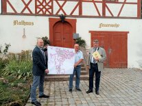 Wolfgang Neukirchner und Ingo Steinbrecher vom Amt für Ländliche Entwicklung Mittelfranken haben Karl Fickel, Bürgermeister von Gerolfingen, einen Zuwendungsbescheid über EU-Fördermittel überreicht. Drei Straßen im Ortskern von Aufkirchen im Landkreis Ansbach sind aktuell nicht gut in Schuss. Mehr Grün sollen das Erscheinungsbild verschönern und neue Parkplätze für mehr Verkehrssicherheit sorgen.